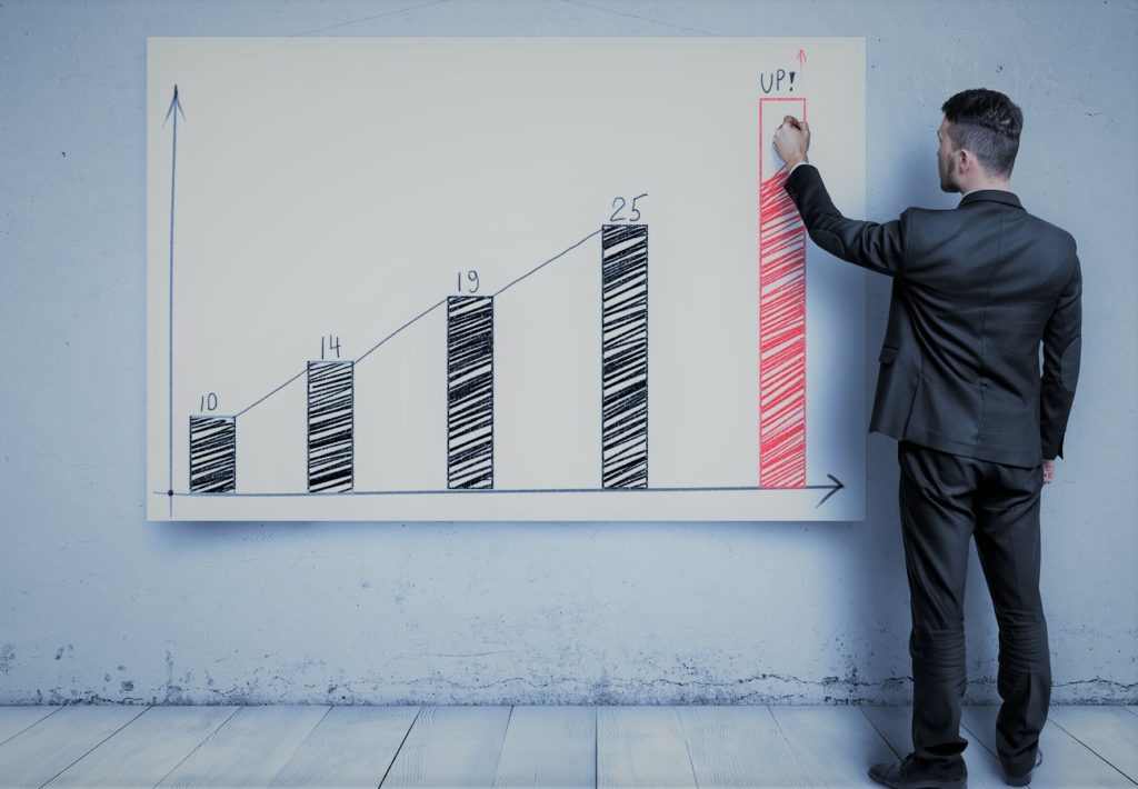 Businessman drawing an upward growth chart with rising bars and an “up” arrow. 