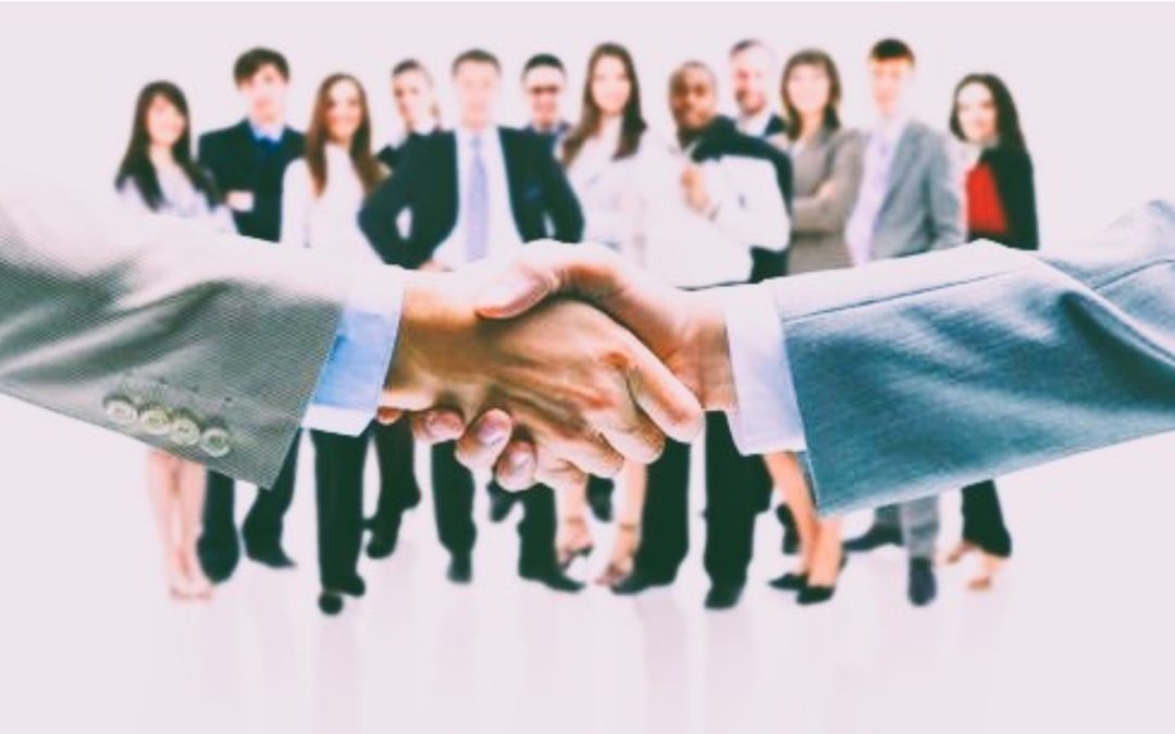 Business professionals shaking hands in front of a team, representing a healthcare acquisition partnership.